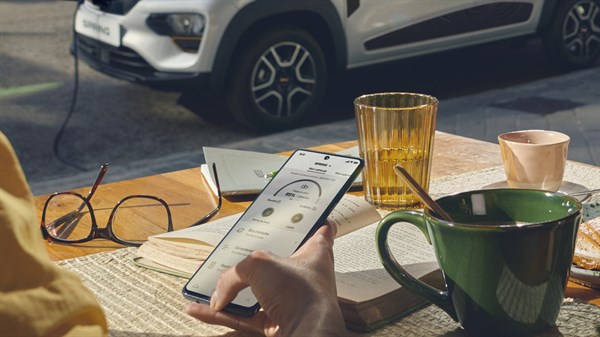 a woman sitting in a table with her hot drink and use the dacia spring app on her smartphone